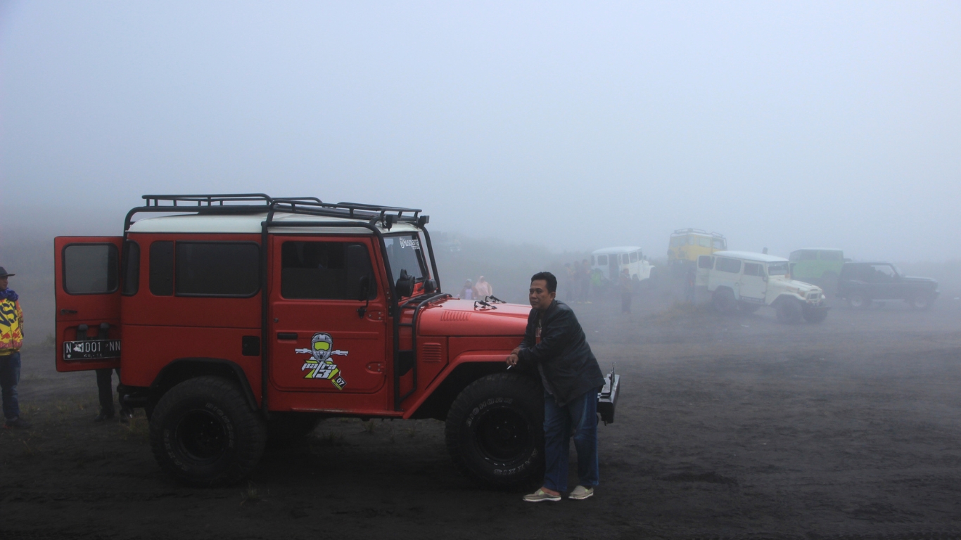 Wisatawan berpose di depan jeep dengan latar armada jeep dan kabut di kawasan Gunung Bromo sebagai bagian dari layanan perjalanan wisata