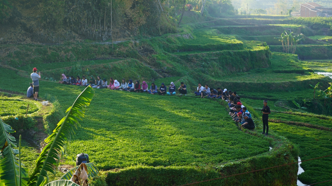 Kegiatan outbound sekelompok wisatawan di area persawahan lereng bukit Batu Malang dengan pemandangan alam terbuka