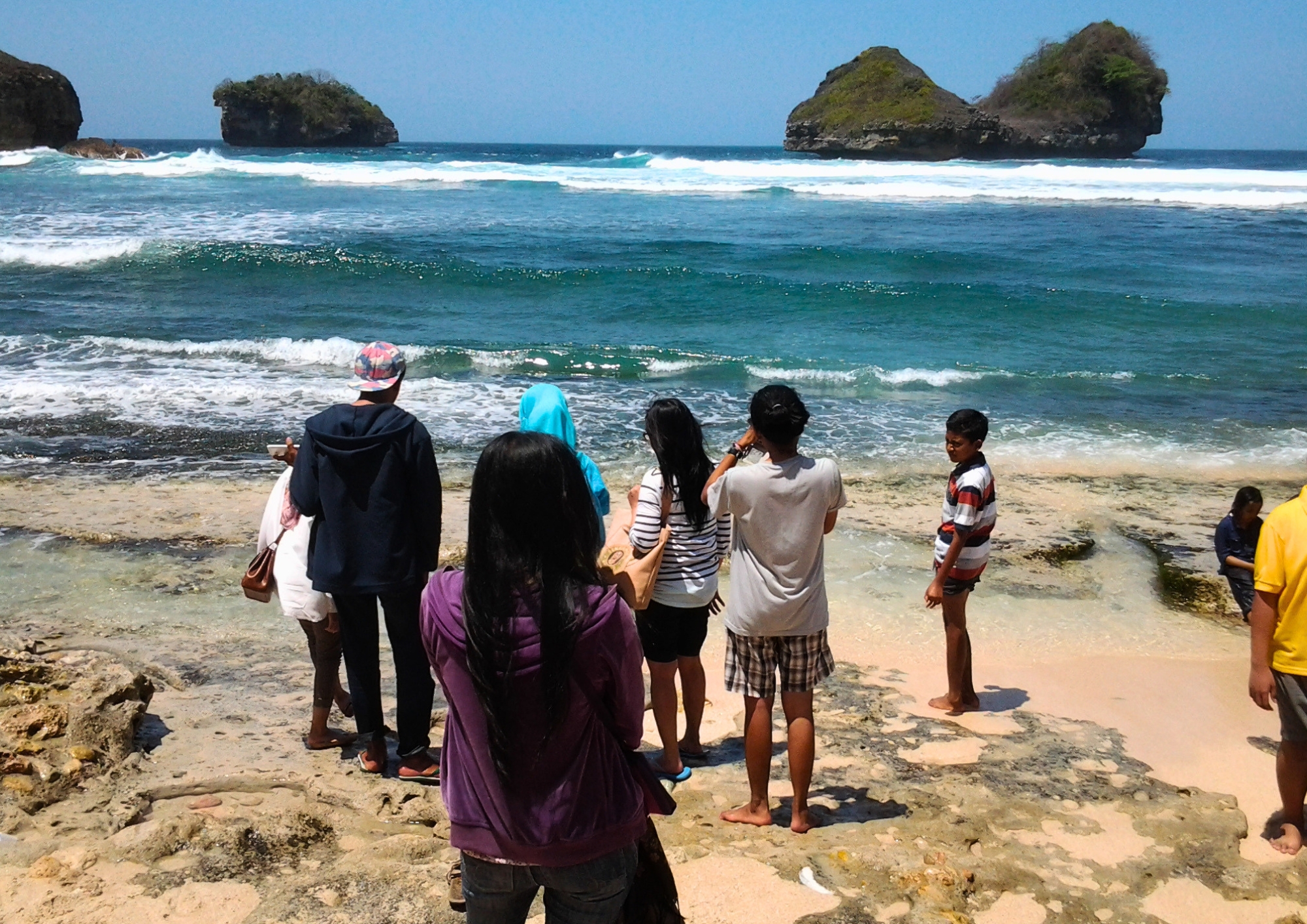 Wisatawan menikmati momen bermain ombak di Pantai Goa Cina sebagai bagian dari pengalaman perjalanan wisata yang tenang dan menyenangkan