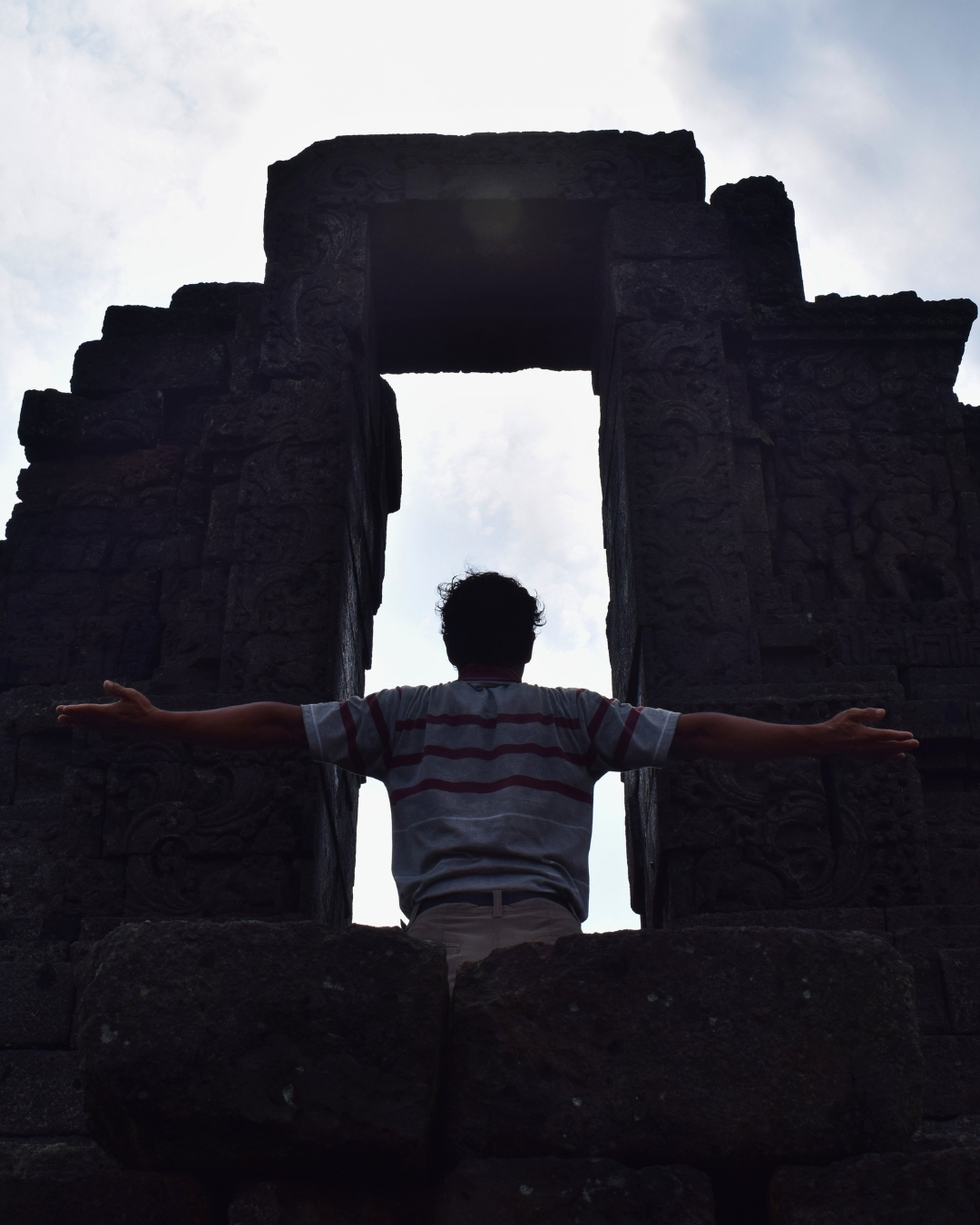 Siluet pengunjung berdoa di depan gerbang Candi Jago Malang dengan sudut low angle dramatis