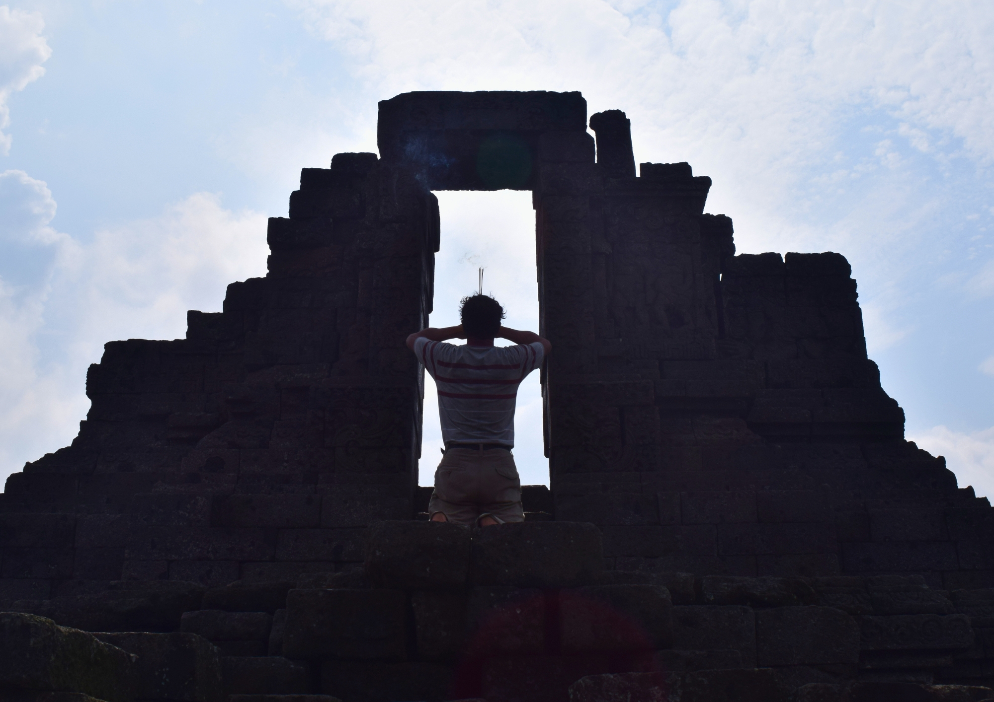 Siluet pengunjung di depan gerbang Candi Jago Malang dengan latar bangunan candi kuno dari sudut low angle